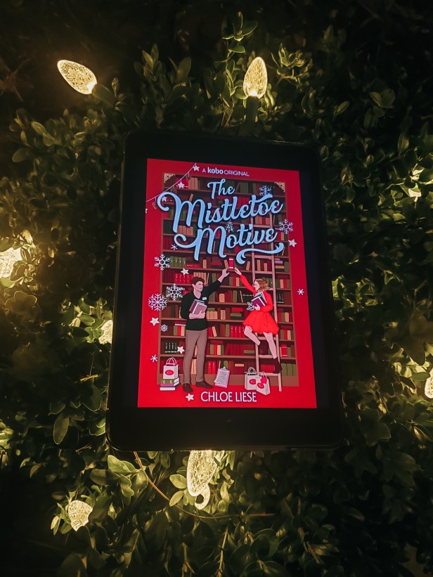 Picture of iPad with The Mistletoe Motive cover, laying on a bush with Christmas lights.